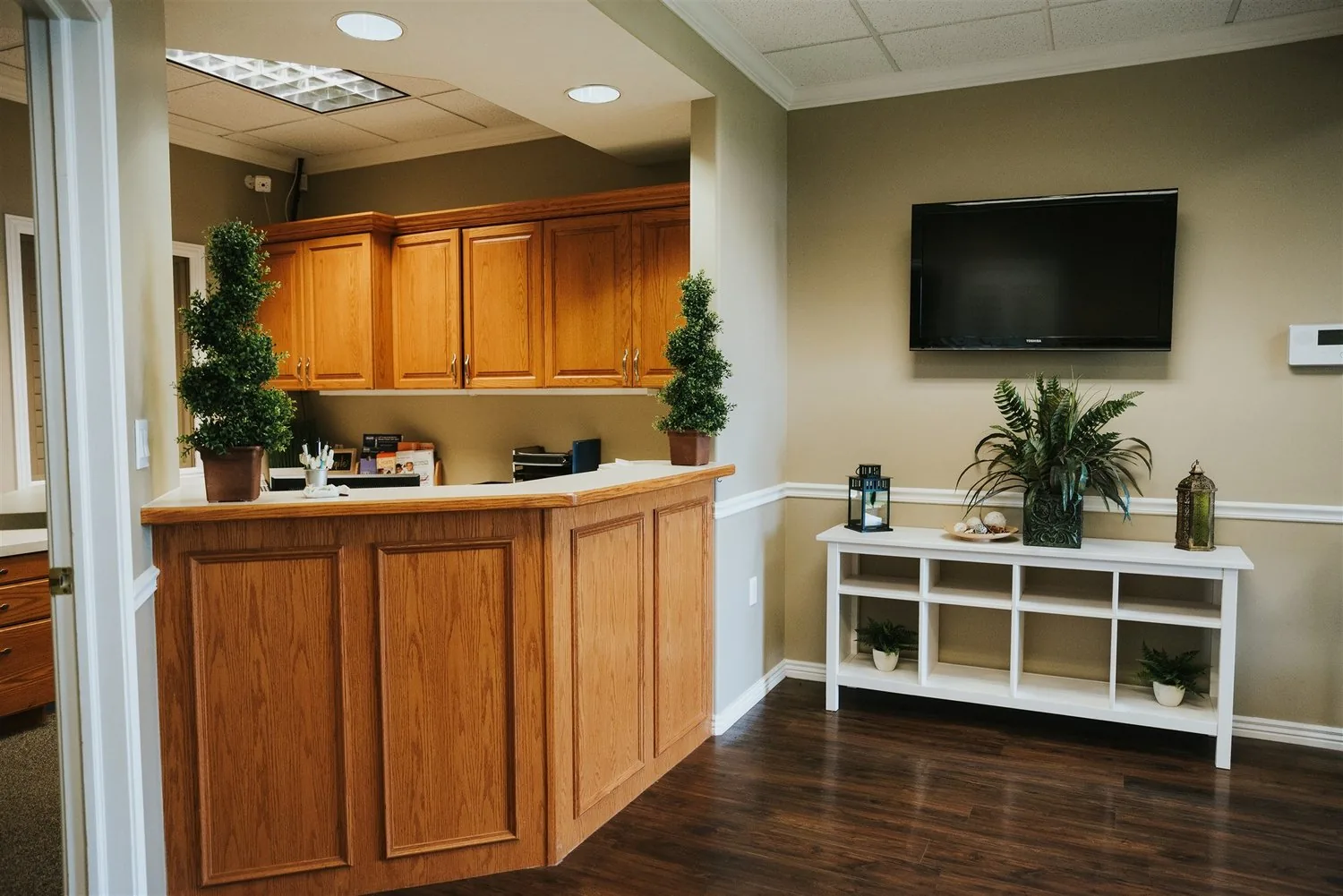 Wooden reception desk and waiting area with a wall-mounted TV and a white display shelf.